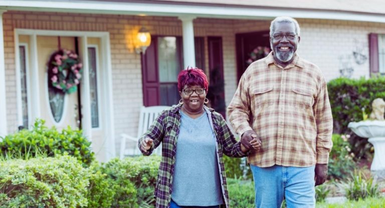 Couple senior souriant marchant devant leur maison aux beaux jours