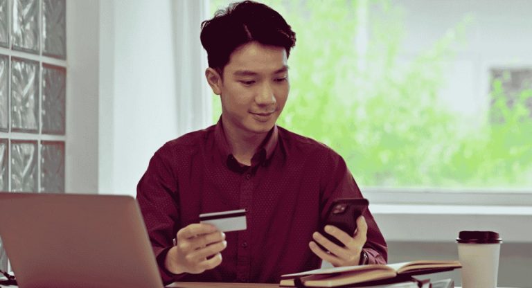 Professionnel saisissant les détails de sa carte bancaire sur un smartphone pour un paiement en ligne depuis son espace de travail