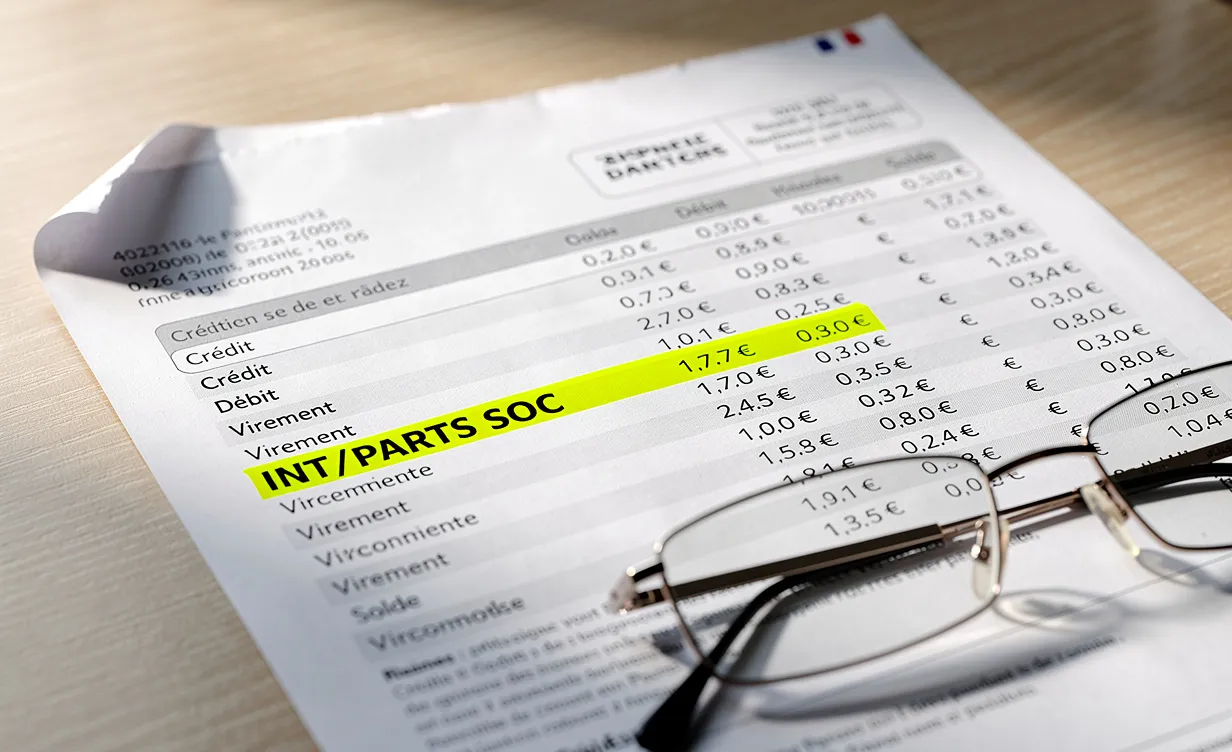 Un relevé bancaire français posé sur un bureau en bois, avec la mention INT/PARTS SOC surlignée et une paire de lunettes à côté.