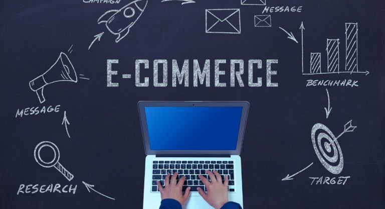 Mains sur un laptop devant un tableau noir avec le mot E-COMMERCE entouré de concepts de stratégie digitale
