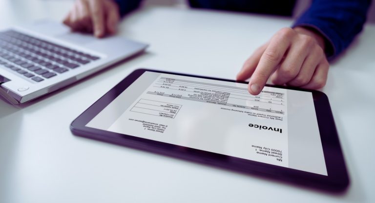 Facture numérique affichée sur une tablette posée sur un bureau à côté d'un ordinateur portable