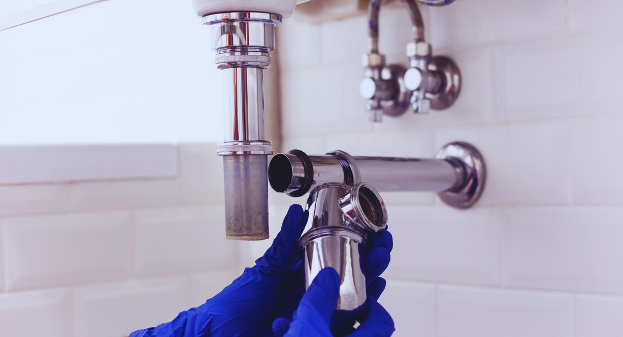 Mains gantées d'un plombier réparant le siphon chromé sous un lavabo de salle de bain