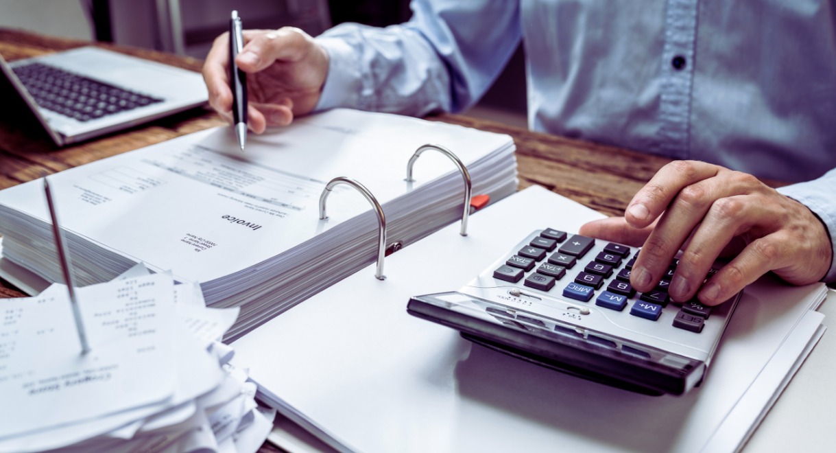 Expert-comptable utilisant une calculatrice devant des classeurs de fiches de salaire et d'invoices