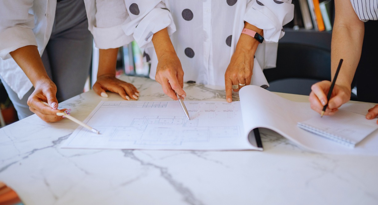 Trois personnes annotent un plan de batiment pose sur une table