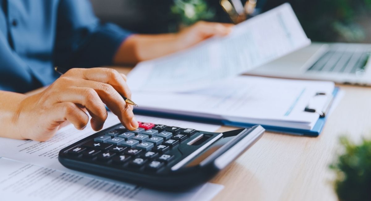 Personne verifiant des documents fiscaux a la calculatrice sur un bureau, stylo en main et ordinateur portable en arriere-plan