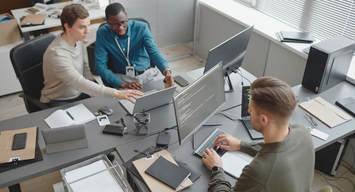 Trois collègues travaillant sur des ordinateurs portables et des écrans affichant du code dans un bureau