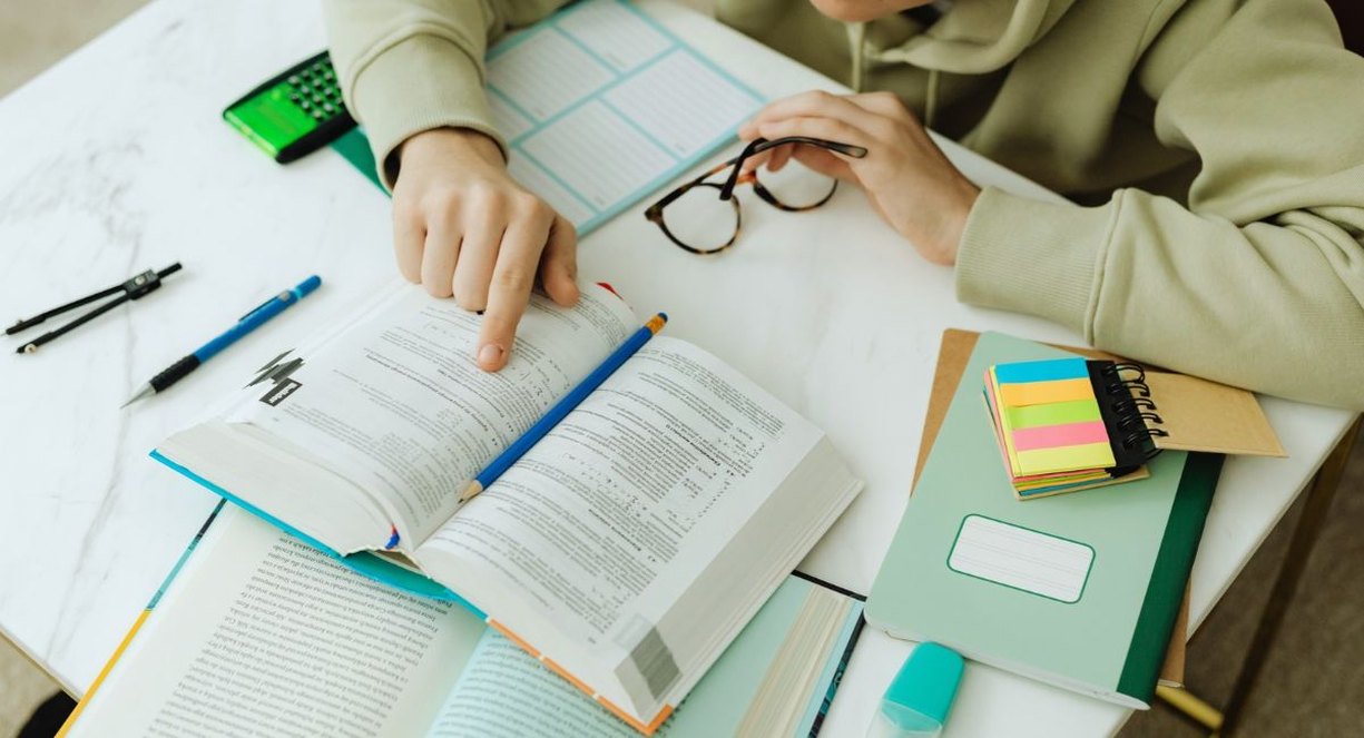 Étudiant révisant un manuel ouvert sur un bureau avec calculatrice, lunettes, cahier et marque-pages colorés